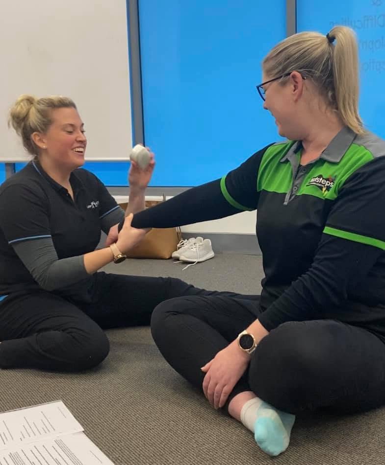 A Little Achievers therapist and an adult client laughing together while practising an arm exercise